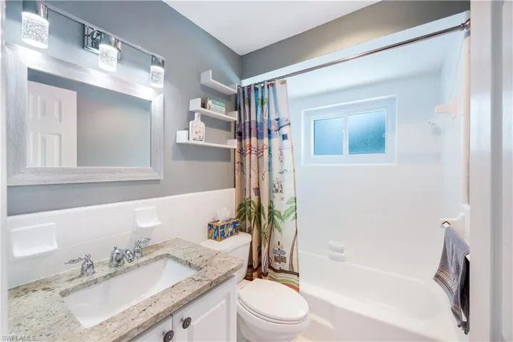 Full bathroom featuring toilet, tile walls, backsplash, shower / tub combo, and vanity