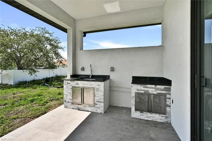 Covered outdoor kitchen area featuring stone veneer cabinetry, dark countertops, a built-in sink, and stainless steel cabinet doors