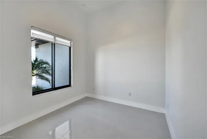 Modern open-concept living space featuring high-gloss tile flooring, a kitchen island with dark countertops, stainless steel appliances, and white cabinetry