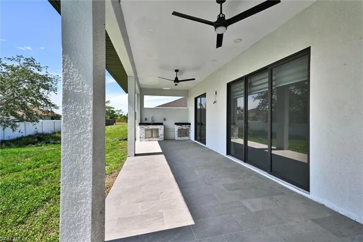 Covered patio featuring large format tile flooring, black ceiling fans with integrated lighting, and multiple sliding glass doors