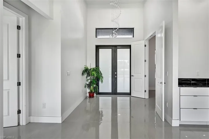 Modern kitchen featuring a large island with a dark countertop, white high-gloss cabinetry, stainless steel appliances, and a unique dark tile backsplash
