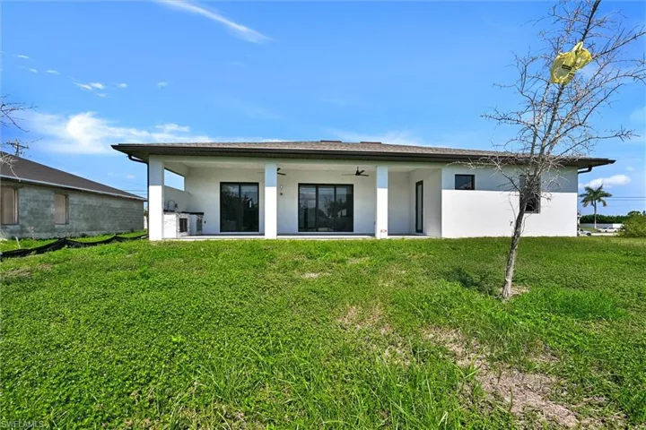 Rear exterior featuring a covered patio with an outdoor kitchen, multiple sliding glass doors, and a ceiling fan