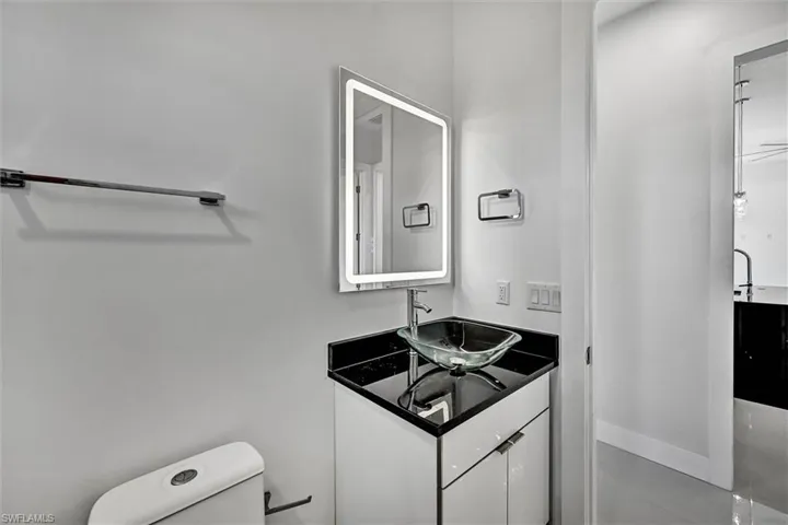 Modern vanity with a vessel sink, black countertop, and an illuminated rectangular mirror