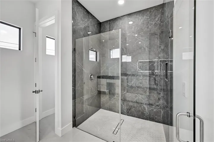 Walk-in shower featuring full-height marble-look tile, frameless glass enclosure, built-in shelving, and a hexagonal tile shower pan
