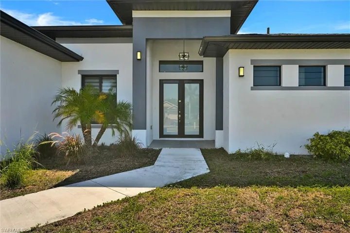 Modern exterior facade featuring a prominent double-door entry with transom window, contemporary wall sconces, dark trim accents, and a concrete pathway