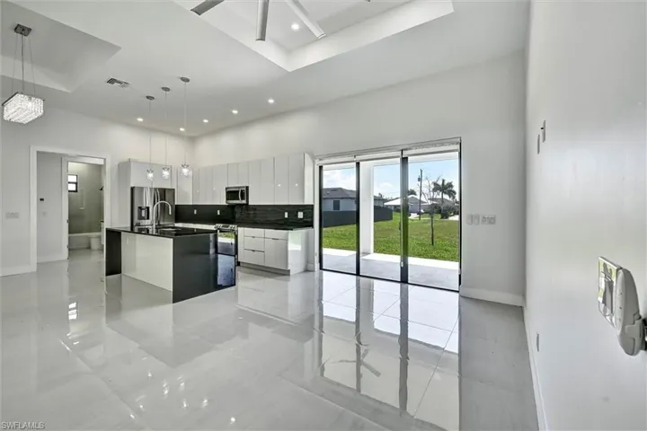Expansive kitchen featuring a large central island with integrated sink and dishwasher, sleek stainless steel appliances, dark countertops, white cabinetry, and high ceilings with recessed lighting