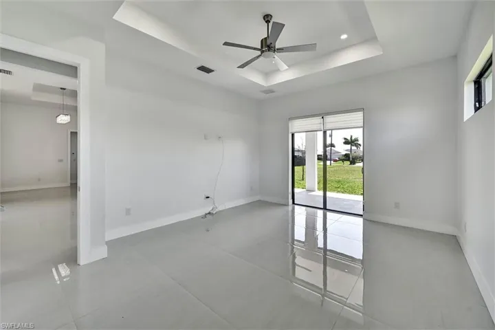Spacious interior room featuring light-toned tile flooring, tray ceiling with recessed lighting, and a ceiling fan