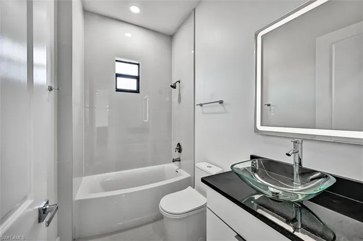 Contemporary bathroom featuring a glass vessel sink, dark countertop, and an illuminated mirror