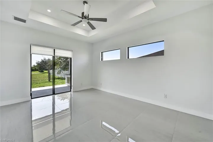 Spacious interior featuring a tray ceiling with recessed lighting and a ceiling fan, polished tile flooring, and a large sliding glass door with blinds