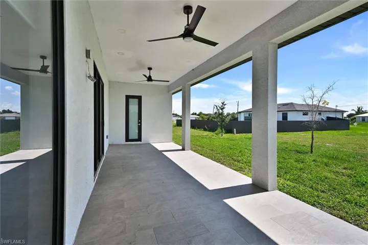 Expansive covered patio featuring large format tile flooring, twin ceiling fans, recessed lighting, and a glass-paneled door