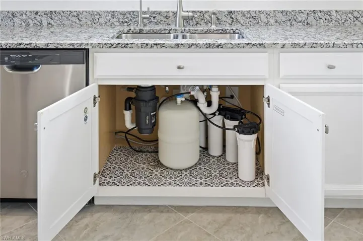 Kitchen view of dishwasher, white cabinetry, and plumbing