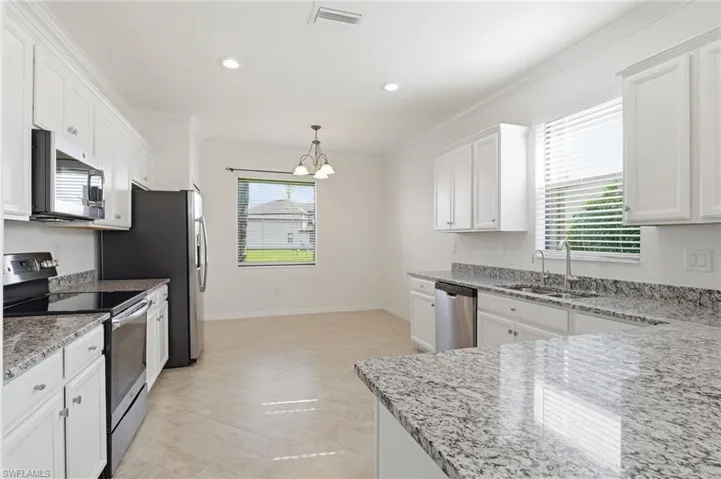 Kitchen featuring stainless steel appliances, white cabinets, light stone counters, ornamental molding, and hanging light fixtures