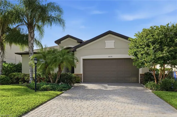 Ranch-style home featuring stone siding, decorative driveway, stucco siding, a front yard, and a garage