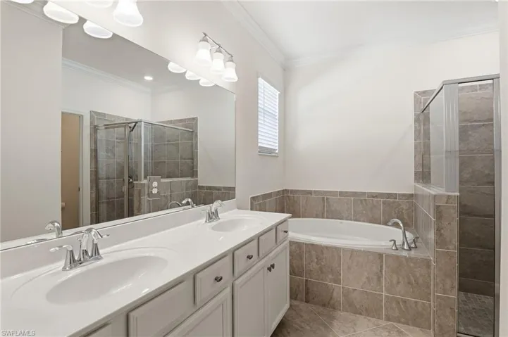 Full bath featuring a garden tub, double vanity, crown molding, a stall shower, and light tile patterned floors