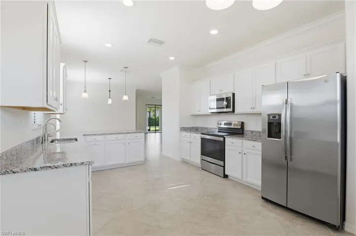 Kitchen with appliances with stainless steel finishes, light stone countertops, white cabinetry, decorative light fixtures, and recessed lighting