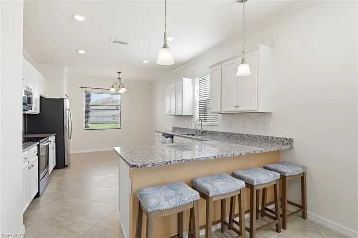 Kitchen featuring a kitchen bar, a peninsula, hanging light fixtures, crown molding, and white cabinets