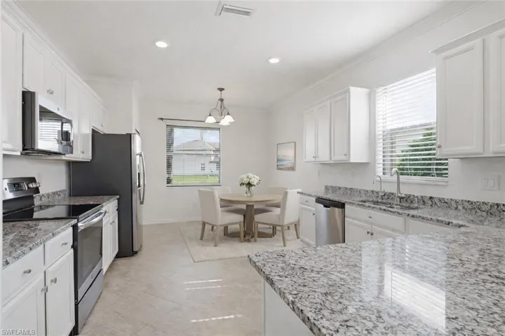Kitchen featuring appliances with stainless steel finishes, white cabinetry, light stone countertops, crown molding, and hanging light fixtures