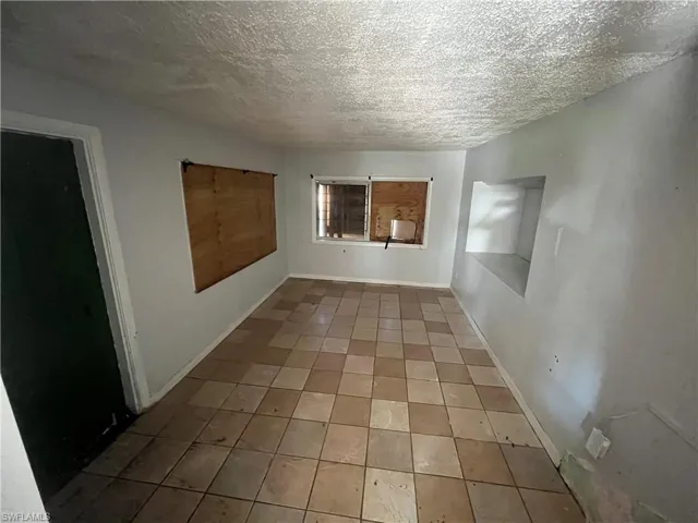 Empty room with tile patterned flooring, a textured ceiling, and baseboards
