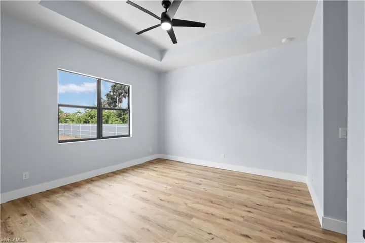 Spare room with a tray ceiling, light wood-style flooring, and a ceiling fan