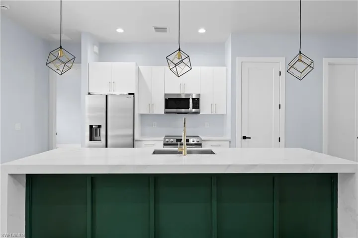 Kitchen with pendant lighting, green cabinets, stainless steel appliances, white cabinetry, and a center island with sink