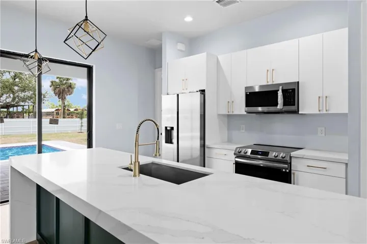 Kitchen featuring pendant lighting, appliances with stainless steel finishes, light stone countertops, white cabinets, and modern cabinets
