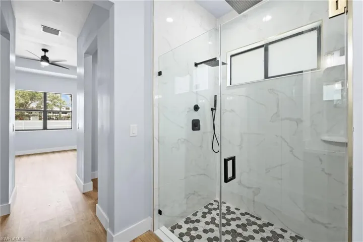 Full bath with a marble finish shower, ceiling fan, and light wood-style flooring