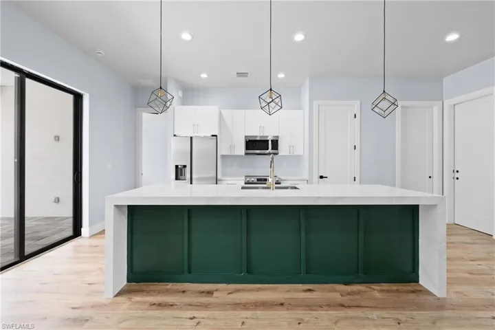 Kitchen with green cabinets, recessed lighting, appliances with stainless steel finishes, white cabinetry, and light wood finished floors