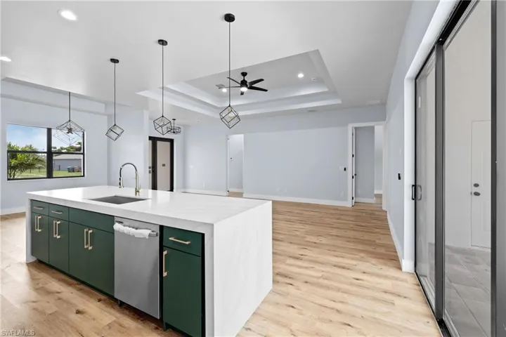 Kitchen with a tray ceiling, open floor plan, an island with sink, green cabinets, and recessed lighting