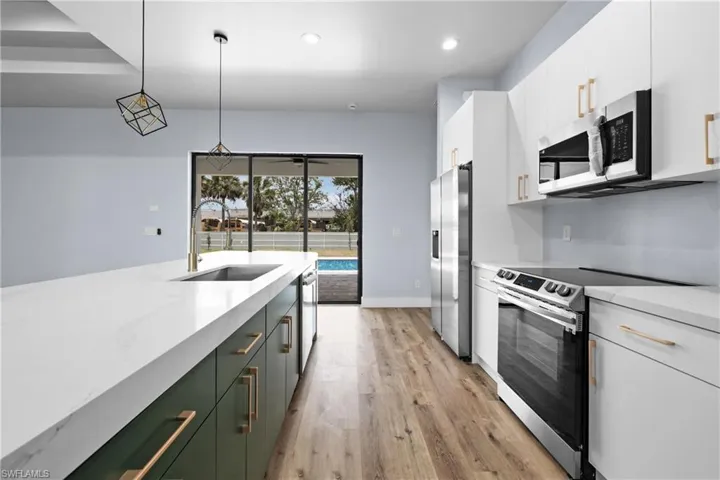 Kitchen with hanging light fixtures, stainless steel appliances, green cabinetry, white cabinets, and light stone counters