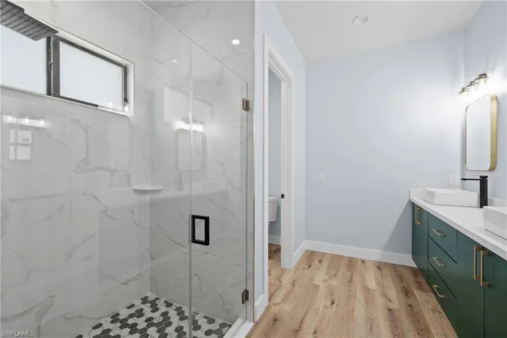 Bathroom with double vanity, a marble finish shower, light wood finished floors, and recessed lighting