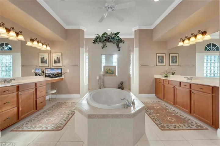 Bathroom with tile patterned flooring, a relaxing tiled tub, ceiling fan, and crown molding