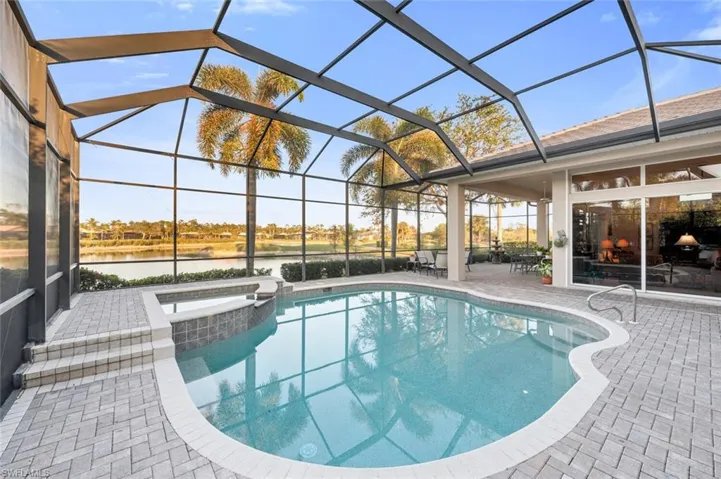 View of swimming pool with glass enclosure, a patio area, a water view, and an in ground hot tub