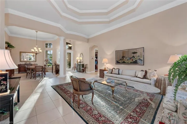 Living room featuring a notable chandelier, a raised ceiling, ornamental molding, and light tile patterned floors
