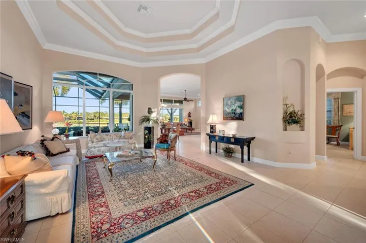Living room featuring a raised ceiling, ceiling fan, light tile patterned floors, and ornamental molding