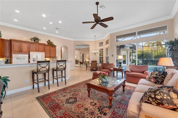 Tiled living room featuring ceiling fan with notable chandelier and crown molding