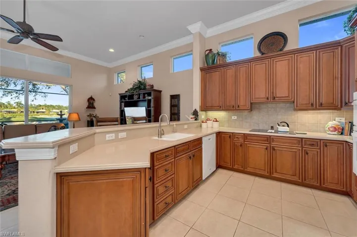 Kitchen with white dishwasher, sink, light tile patterned floors, ornamental molding, and kitchen peninsula