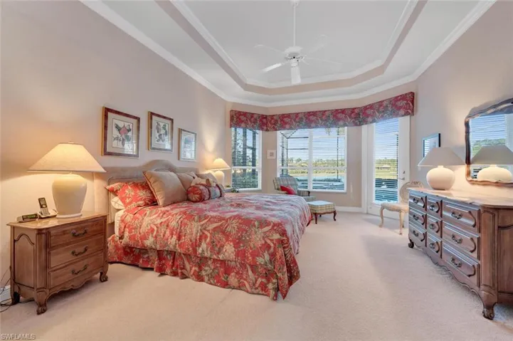 Carpeted bedroom with a raised ceiling, ceiling fan, and crown molding