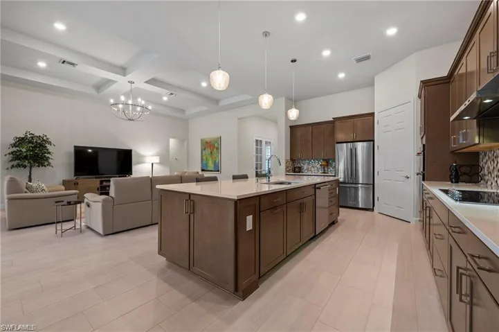Kitchen featuring stainless steel appliances, coffered ceiling, hanging light fixtures, sink, and an island with sink