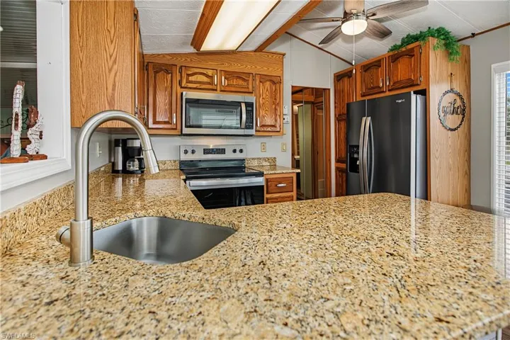 Kitchen featuring stone countertops, stainless steel undermount sink with a gooseneck faucet, wood cabinetry, built-in stainless steel microwave, and stainless steel refrigerator