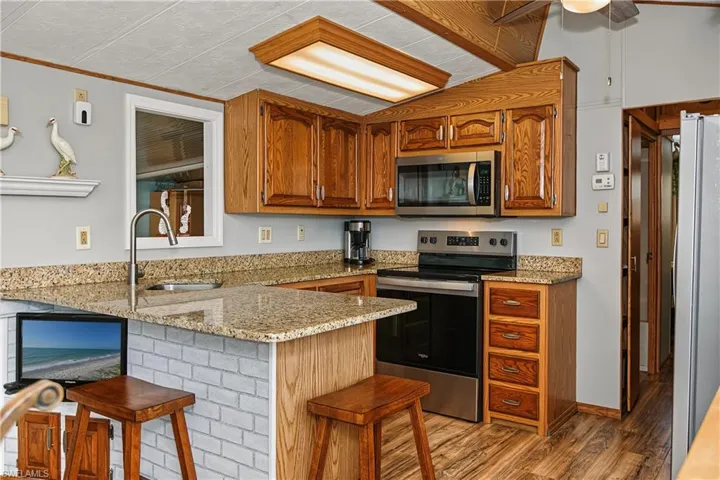 Kitchen featuring stained wood cabinetry, stone-finish countertops, stainless steel appliances, and a brick-patterned peninsula base