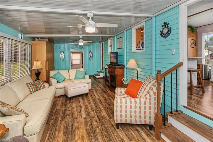 Wood-finish flooring, horizontal panel walls, built-in electric fireplace with mantle, dual ceiling fans, and wood-finish staircase with metal balusters