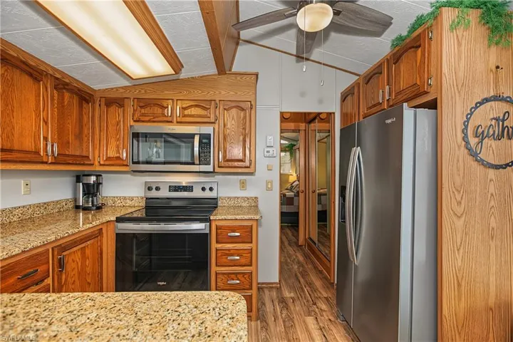 Kitchen featuring oak cabinetry, stone-finish countertops, stainless steel appliances, wood-finish flooring, and a ceiling fan