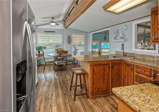 Kitchen featuring wood cabinetry, stone-finish countertops, stainless steel refrigerator, ceiling fan, and wood-finish flooring