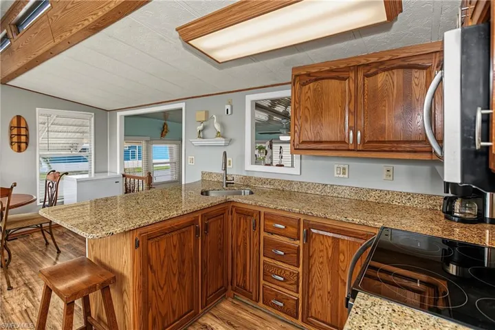 Kitchen featuring wood cabinetry, stone-surface countertops, wood-finish flooring, exposed ceiling beams, and a stainless steel undermount sink