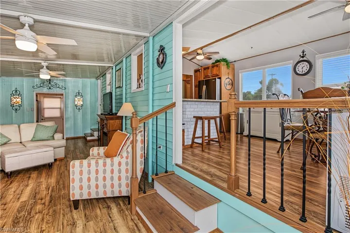 Wood-finish flooring, light blue horizontal paneled walls, tiered levels with wood-top stairs, and breakfast bar with white brick-style base