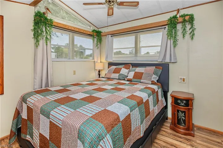 Room featuring wood-finish flooring, vaulted ceilings, a ceiling fan, and multi-paned windows with integrated horizontal blinds