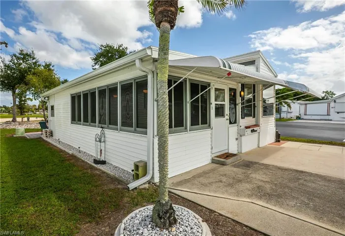 White exterior siding featuring an enclosed screened porch, metal awning, and concrete driveway
