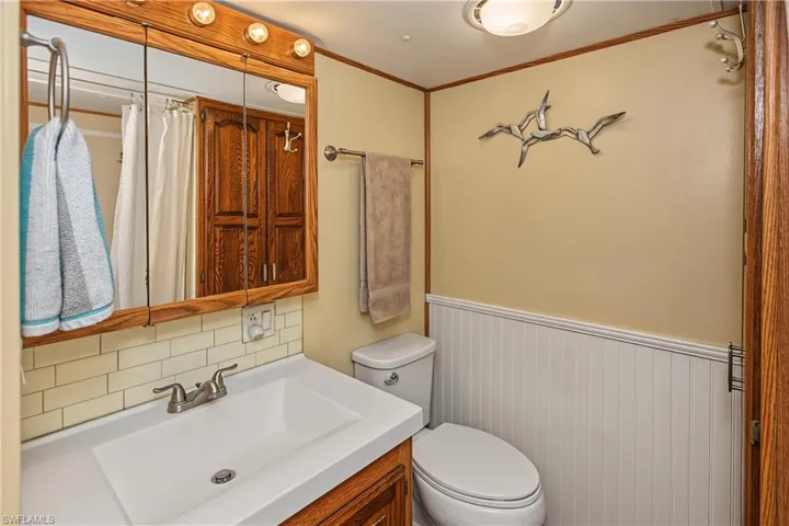 Bathroom featuring a wood-frame medicine cabinet, subway tile backsplash, white beadboard wainscoting, and a two-handle metal faucet
