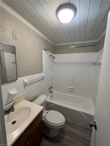Full bath with shower / bath combination, vanity, ornamental molding, tile walls, and wood finished floors
