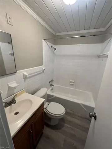 Full bath featuring washtub / shower combination, ornamental molding, vanity, dark wood-type flooring, and tile walls